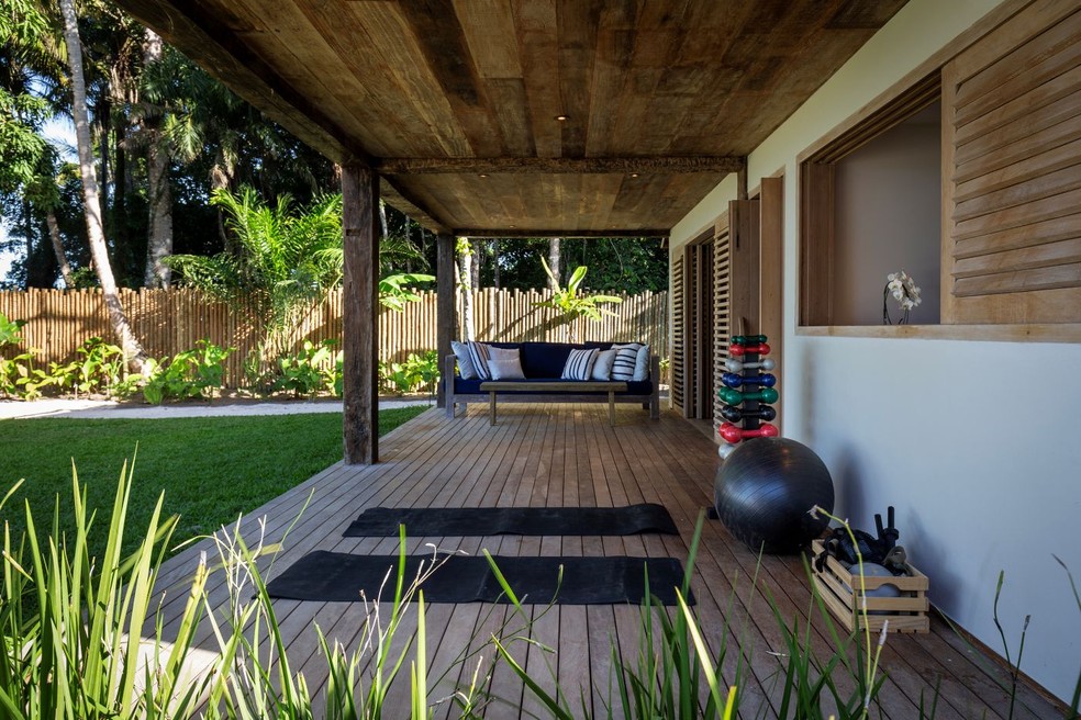 VARANDA DOS QUARTOS | O deque de madeira estabelece continuidade entre a suíte e o jardim, transformando-se num local para contemplação e prática de exercícios ao ar livre. O banco estofado foi desenvolvido pelo escritório e executado pela Casa do Lírio. Esquadrias de madeira da Marcenaria Arte Nativa — Foto: Antonio Soto/Divulgação