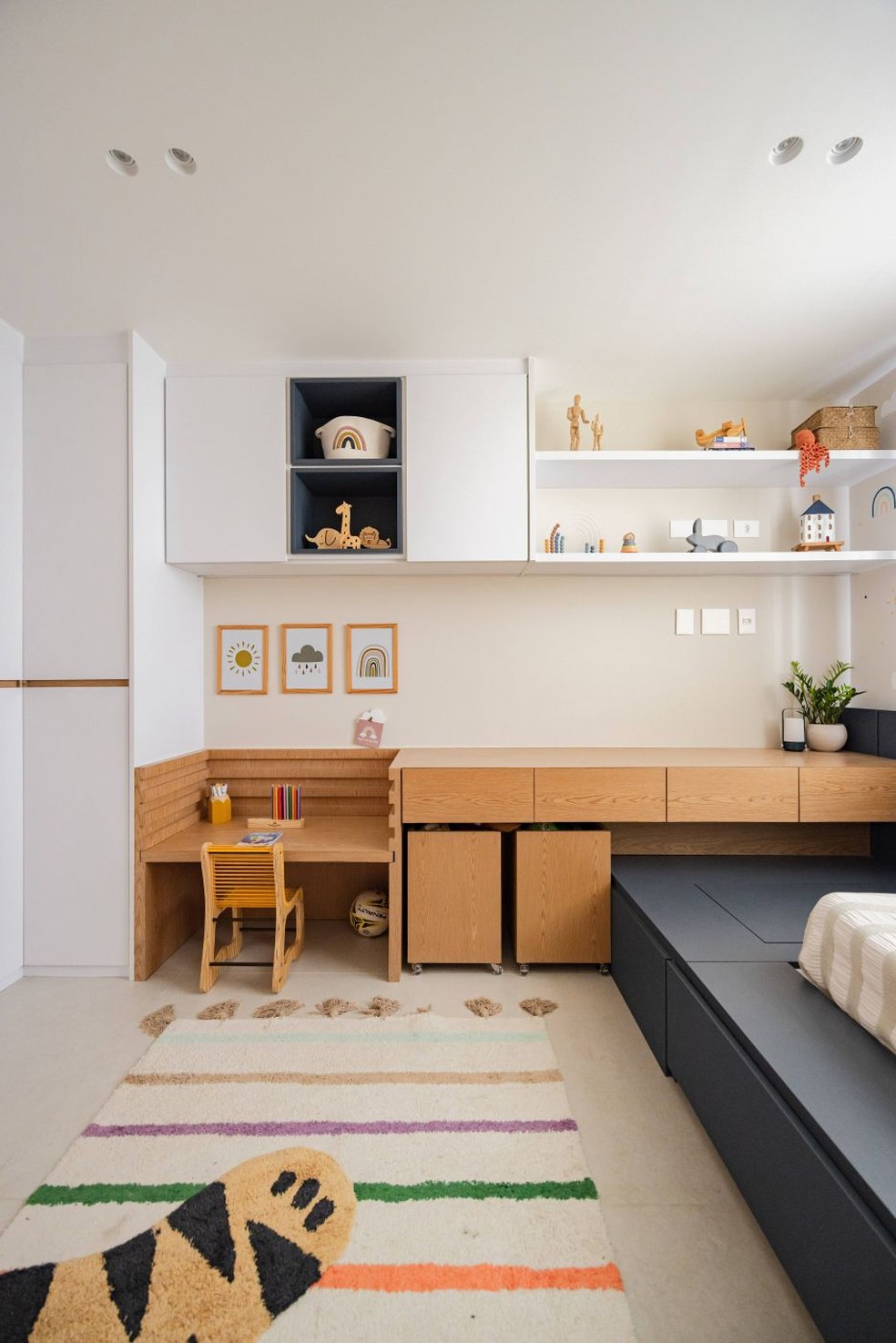 QUARTO INFANTIL | Do outro lado do quarto, a marcenaria em MDF branco e lâmina de carvalho-americano reúne armários, prateleiras e uma mesa evolutiva, pensada para acompanhar o crescimento da criança. A cadeira é da Woodenland Design, comercializada pela Boobam, e o tapete de tigre é da Uauá Kids — Foto: Pedro Mello/Interior da Foto/Divulgação