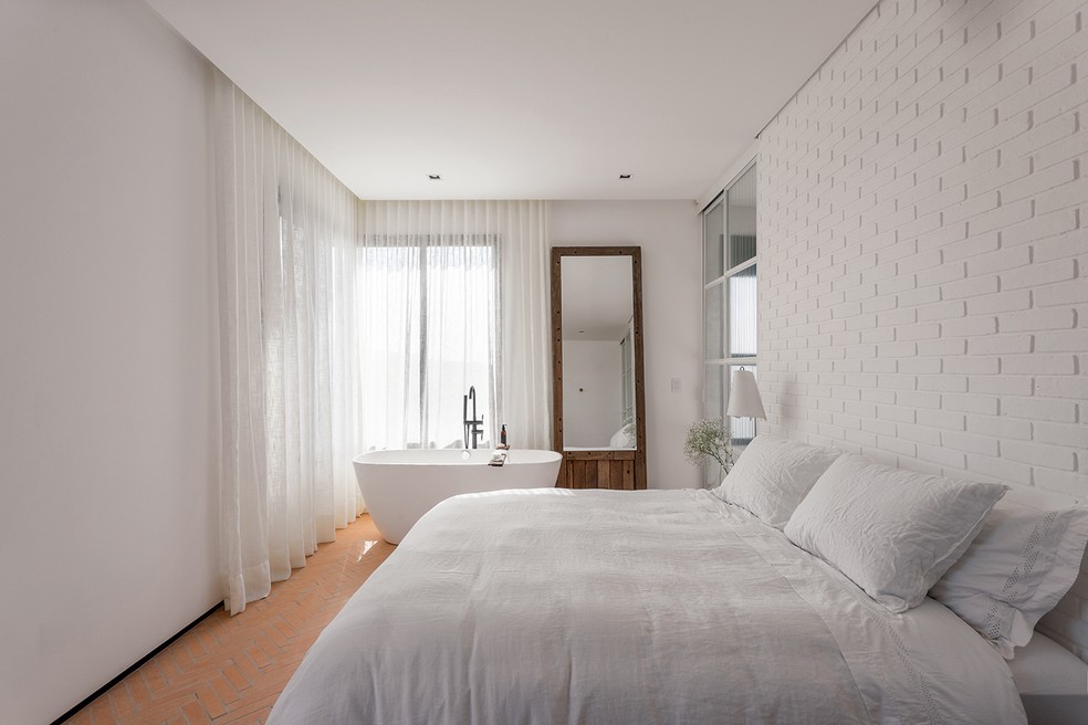 Seladores e produtos de proteção indicados para cada revestimento podem ajudar a facilitar a limpeza e conservar a superfície. No quarto, a parede de tijolo de barro pintado de branco faz as vezes de cabeceira — Foto: Thiago Travesso/Divulgação | Projeto da arquiteta Carolina Miluzzi